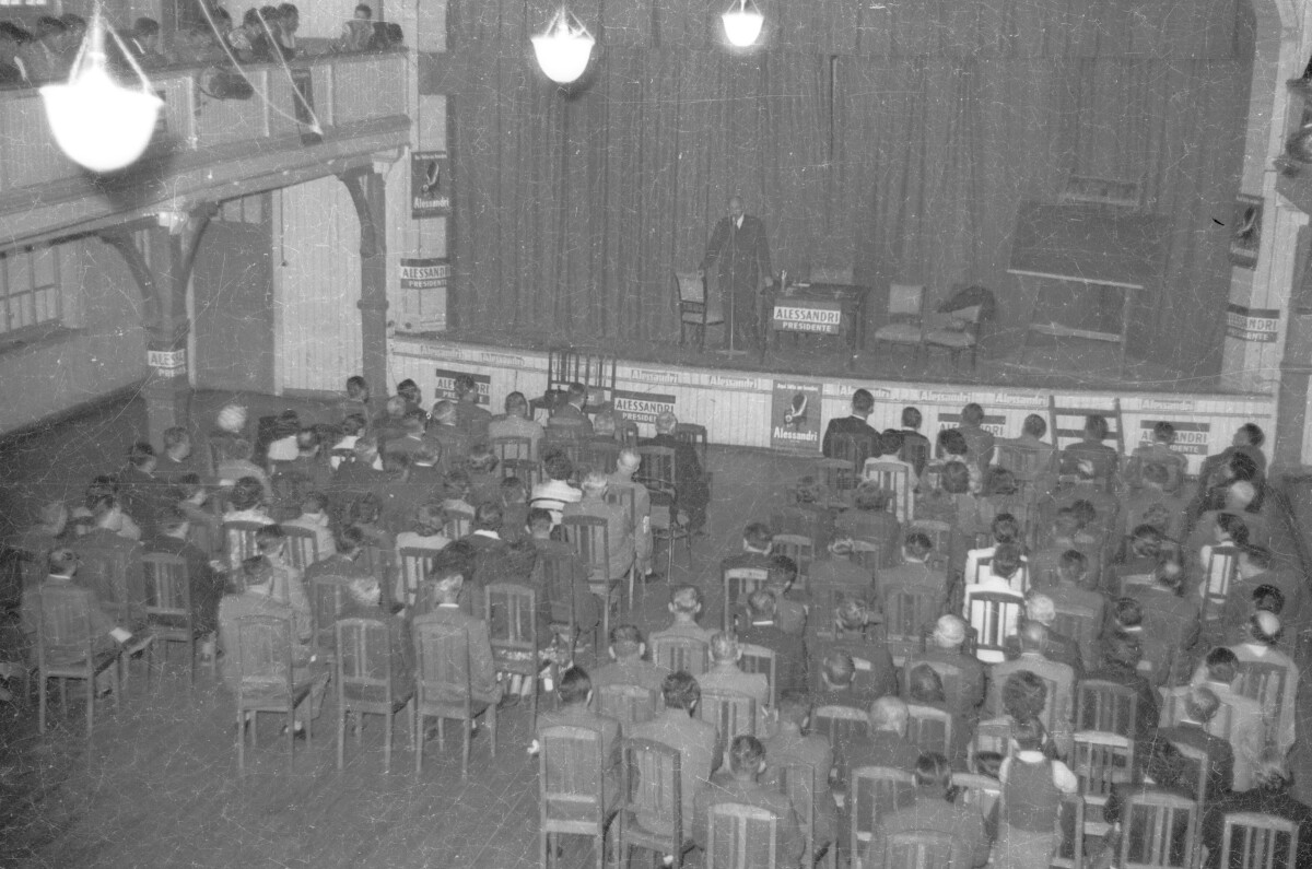 plano general desde un punto alto hacia un grupo de Hombres que se encuentran observando el discurso realizado por Jorge Alessandri, durante su candidatura presidencial realizada en la ciudad de La Unión