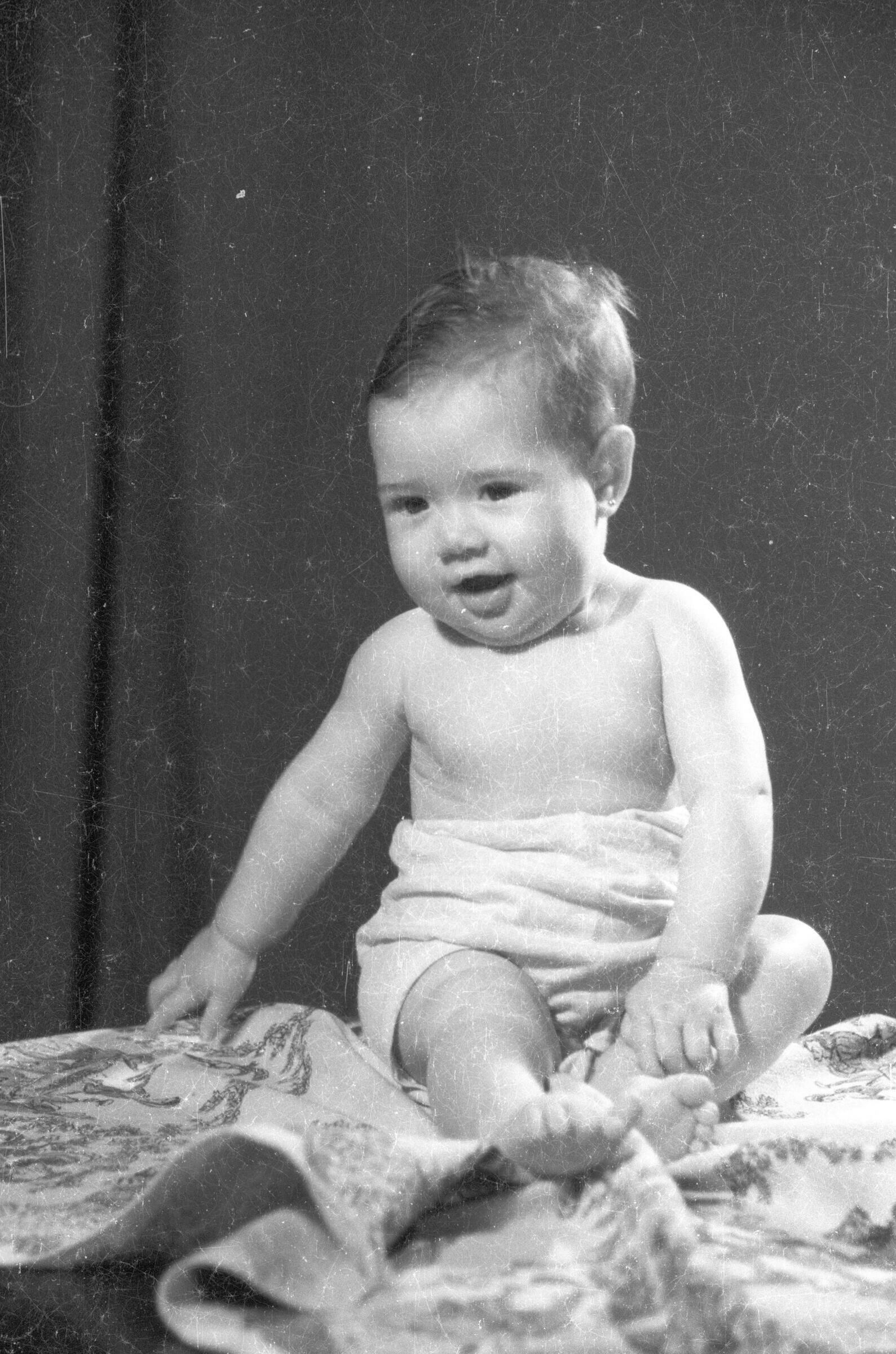 Retrato de estudio de Plano entero de un bebé semidesnudo, sonriendo mientras se encuentra sentado sobre una mesa