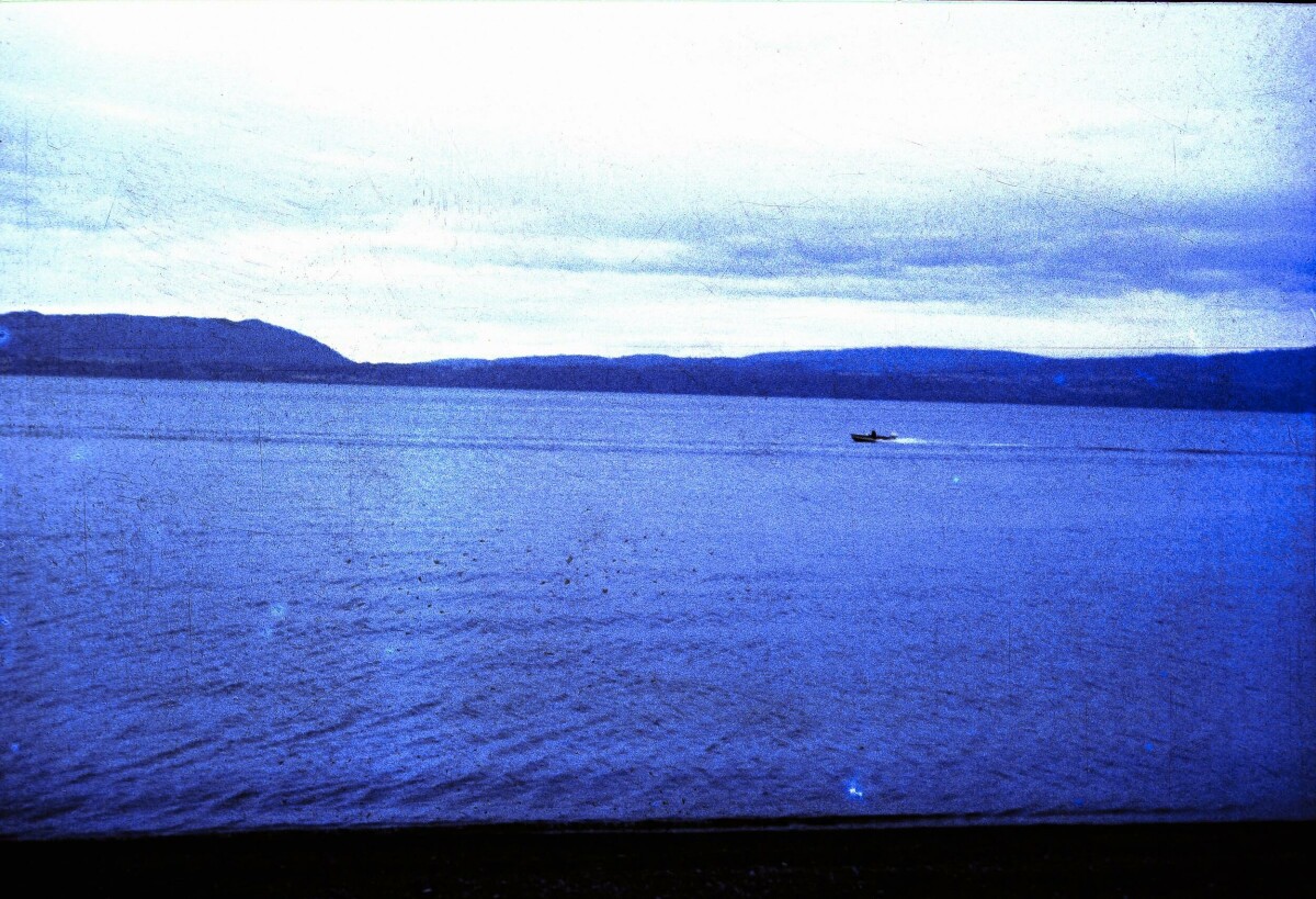 plano general de una lancha navegando por un lago rodeado de cerros