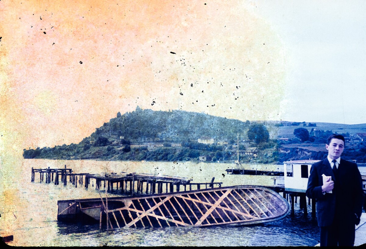 Retrato de plano medio de Hombre con Traje posando de frente, detrás de él un lago y un muelle que al parecer está en mal estado