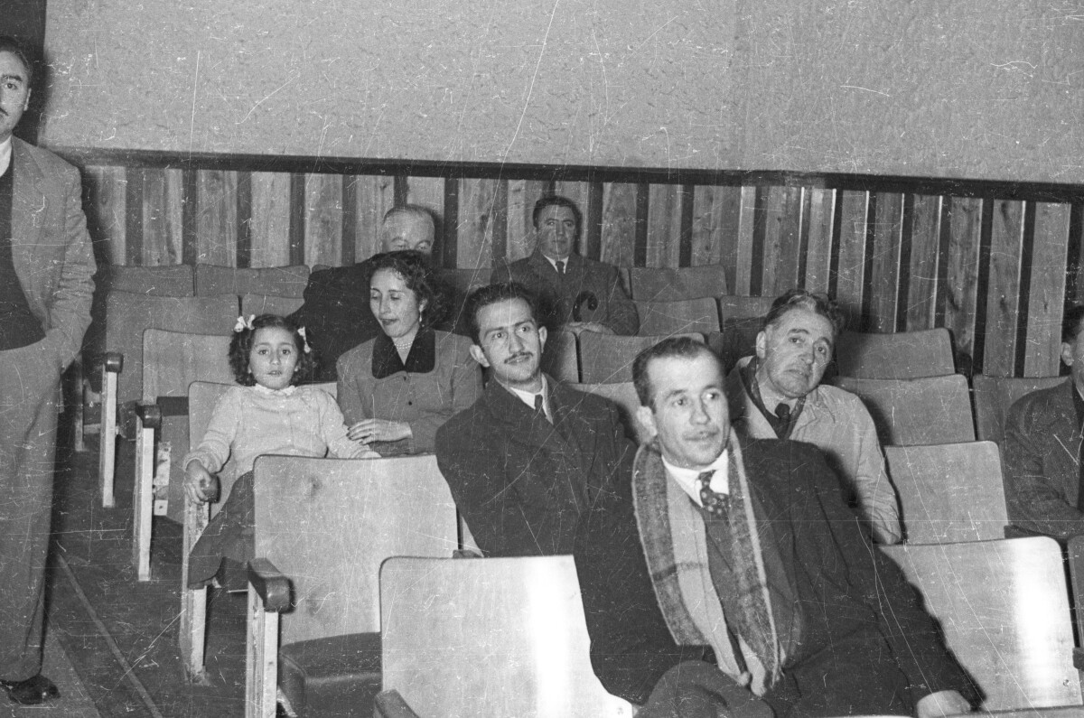 plano general de un grupo de Hombres, Mujer y un niña sentados en unas butacas mientras observan un espectáculo en el interior del teatro O'Higgins de La Unión