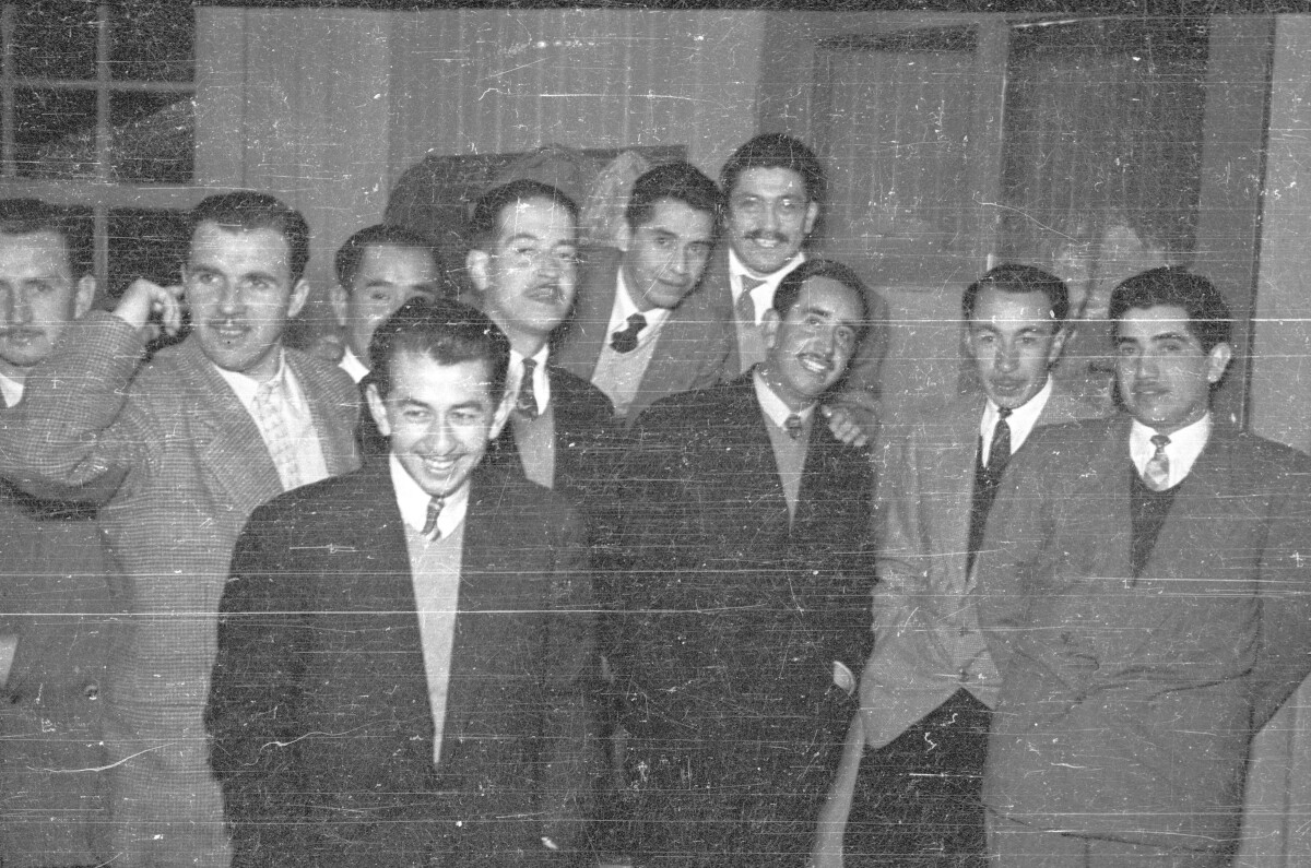 Retrato grupal de plano entero de Hombres posando juntos, todos llevan puesto un traje, están en el interior de un local