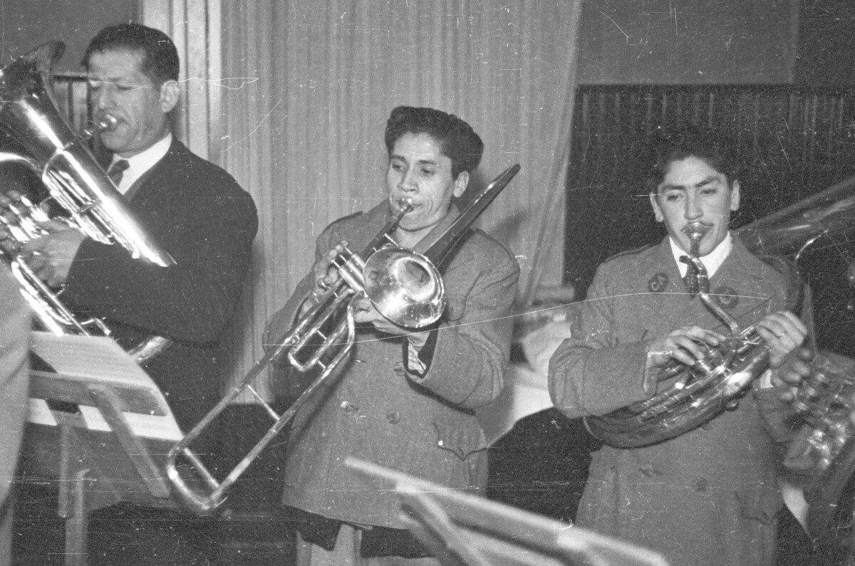 plano general de tres hombres tocando instrumentos durante una celebración en el interior de un local