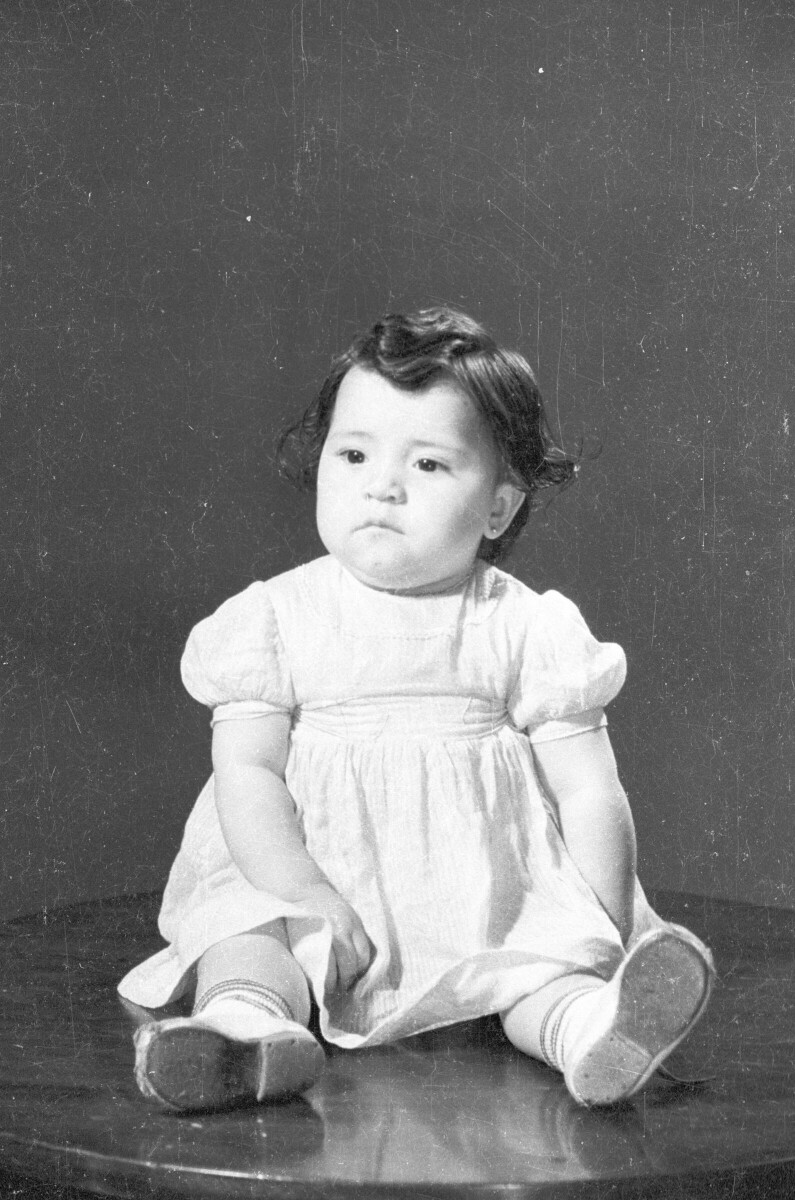 Retrato de estudio de Plano entero de Bebé con Vestido sentada sobre una mesa, mirando hacia el lado