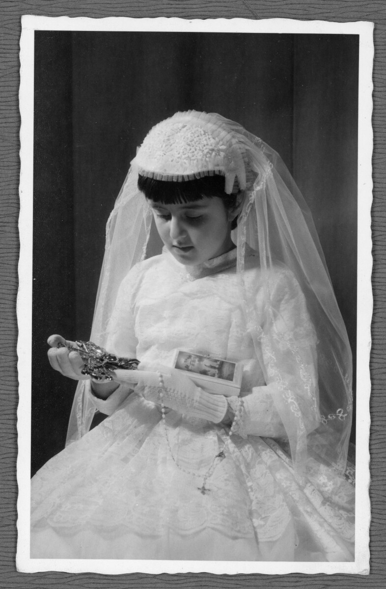 Retrato de niña con atuendo de primera comunión, sosteniendo un crucifijo y un rosario