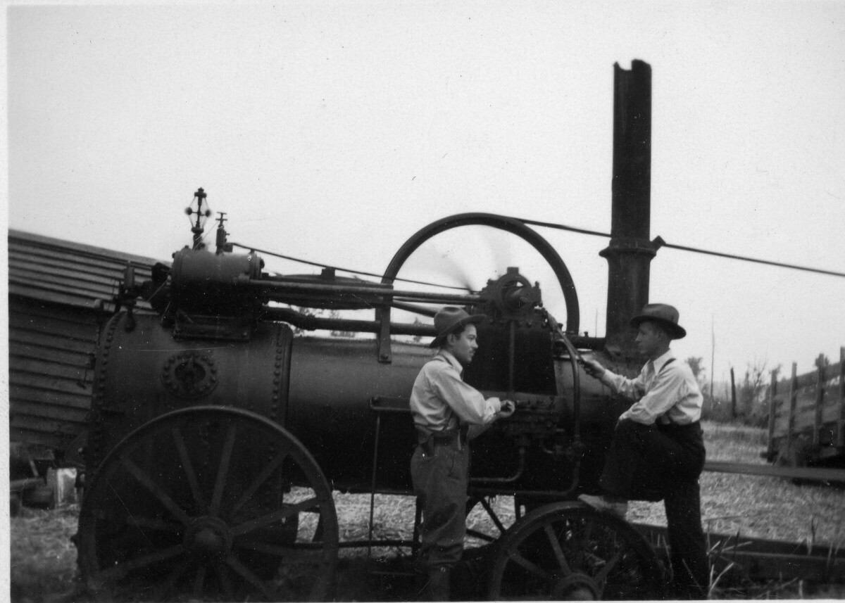 plano general de dos hombres con sombrero, conversando a un costado de un locomóvil en una zona rural no identificada