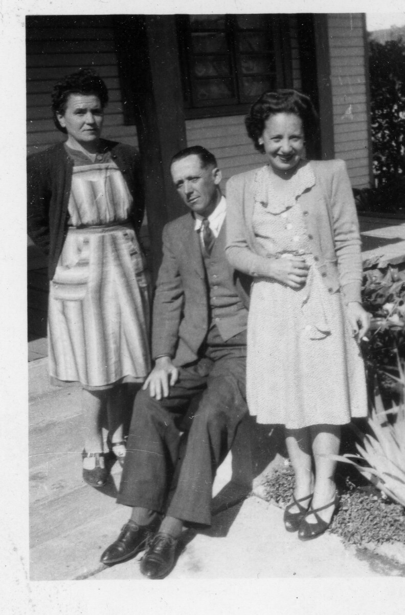 Retrato de plano entero de dos mujeres y un hombre posando. El hombre viste de Traje y las mujeres llevan puesto un Vestido. Se encuentran en el frontis de una casa.