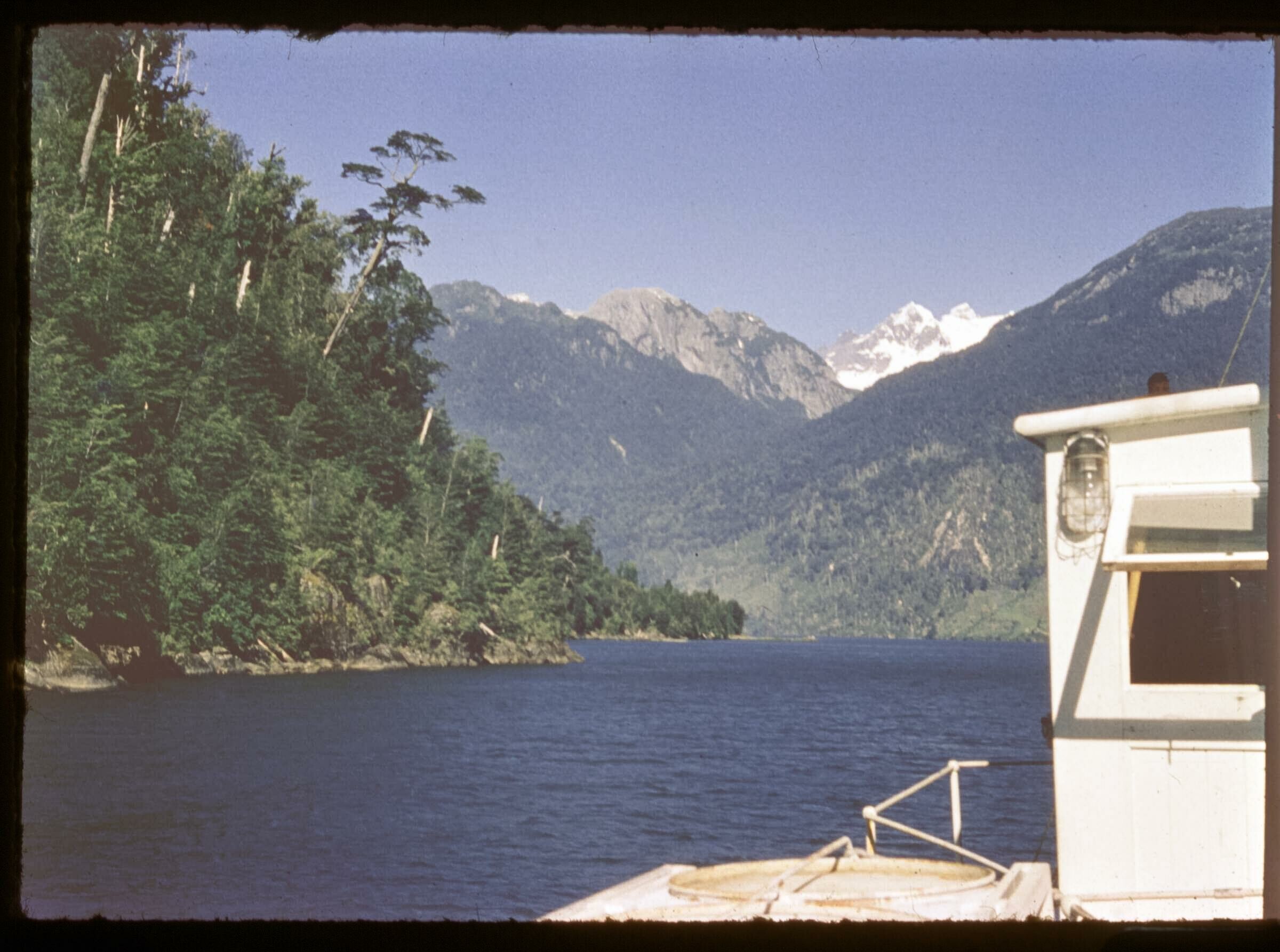 Plano entero de la parte superior de un barco navegando por un lago rodeado de montañas