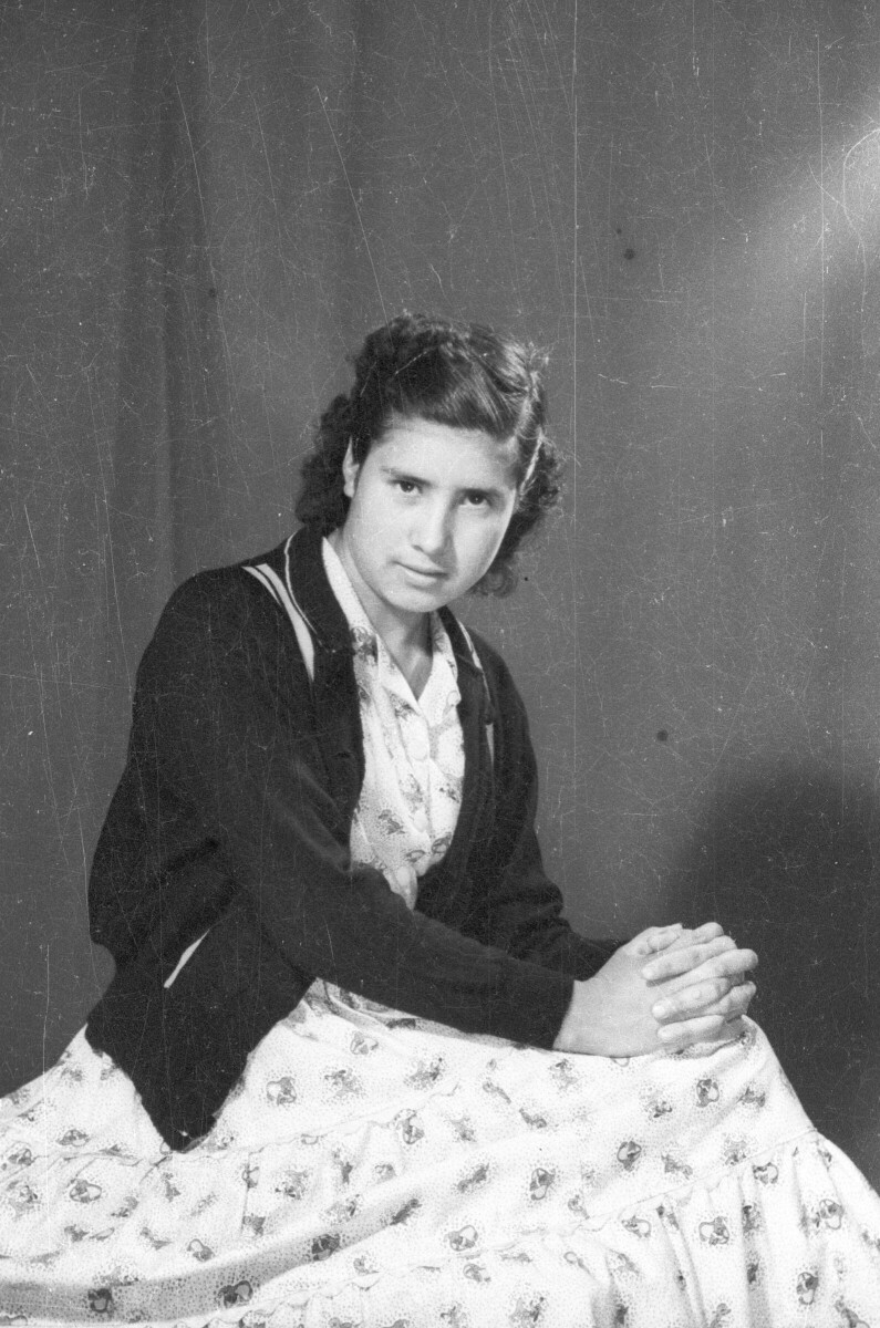 Retrato de estudio Plano americano de Mujer sentada de lado con manos en las rodillas, mirando de frente