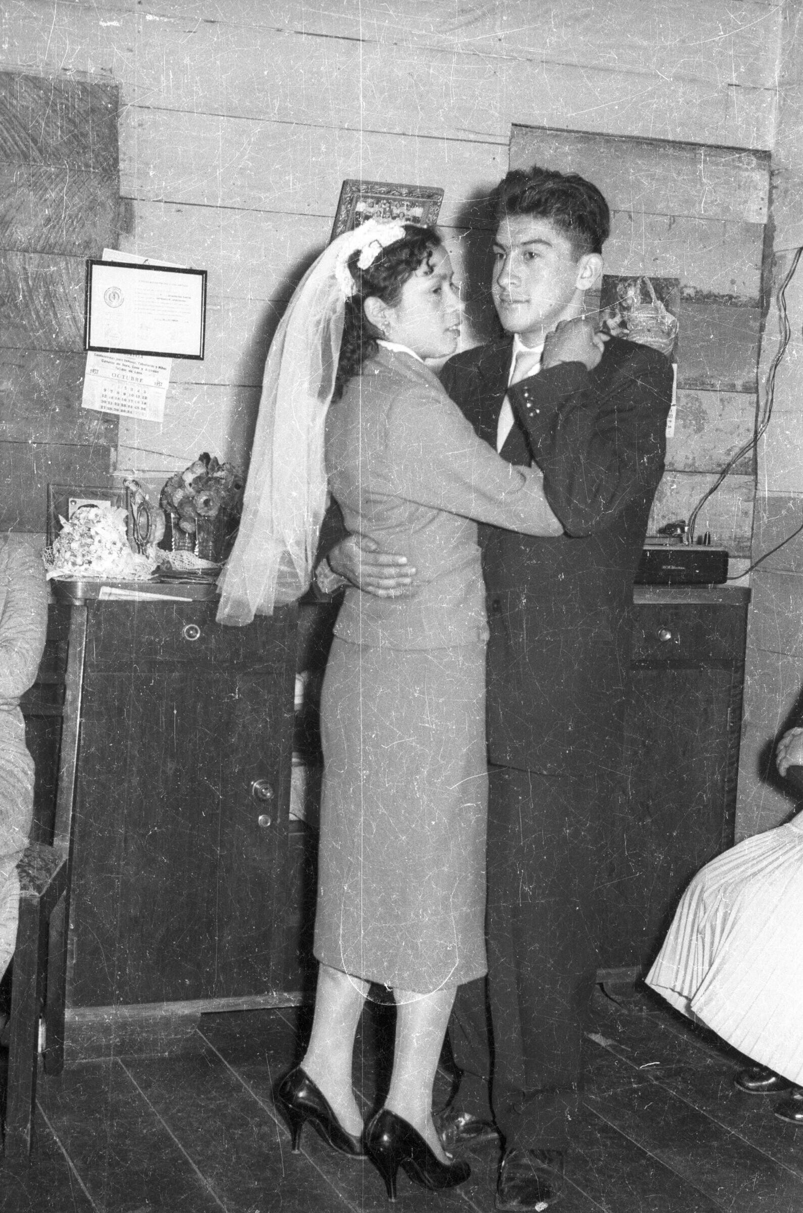 Plano entero de una pareja de recién casados bailando tomados de la mano, durante la celebración de su casamiento realizada en el interior de una casa