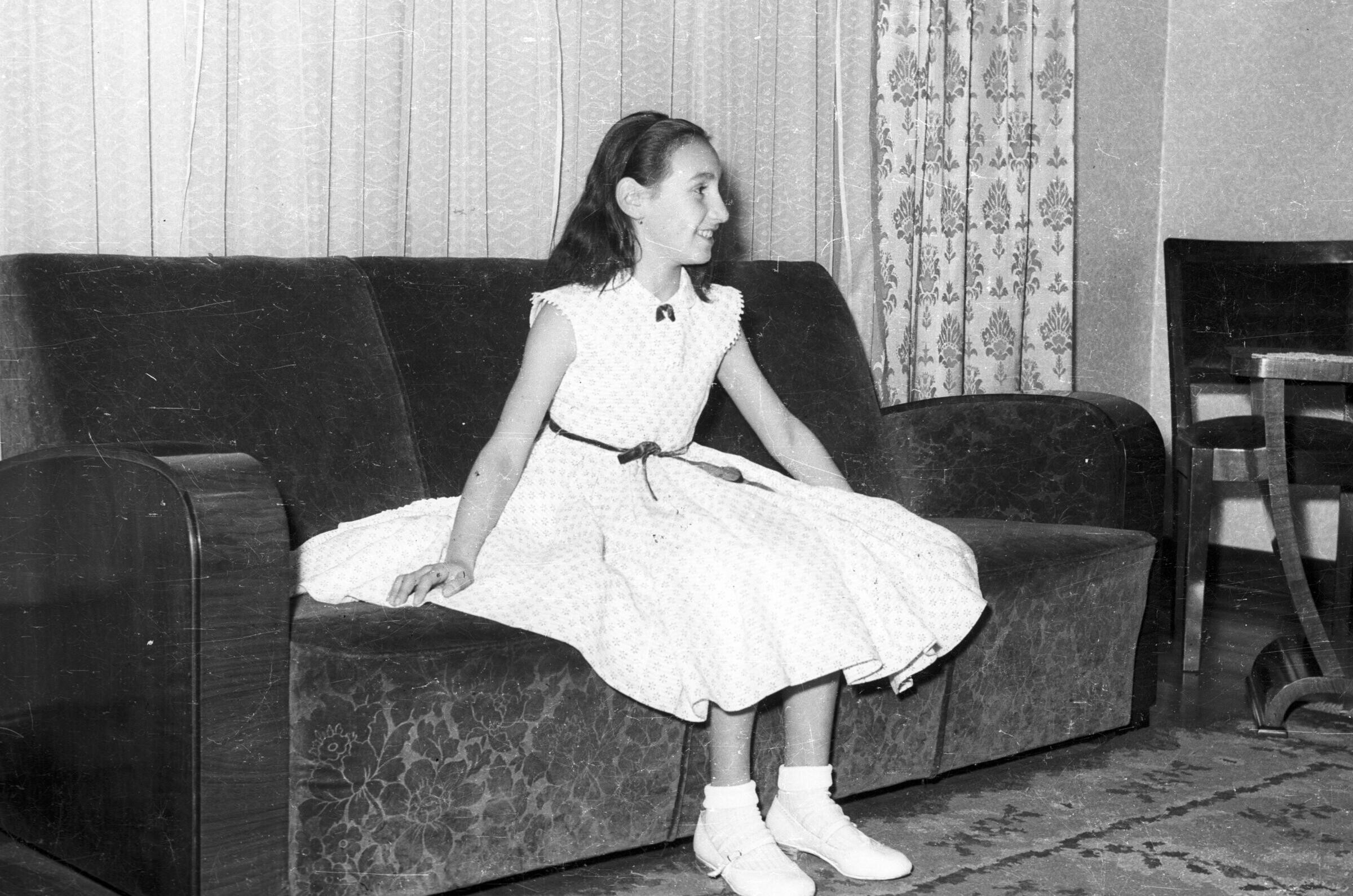 Plano entero de una Niña con Vestido, posando parada junto a una chimenea en el interior de una casa