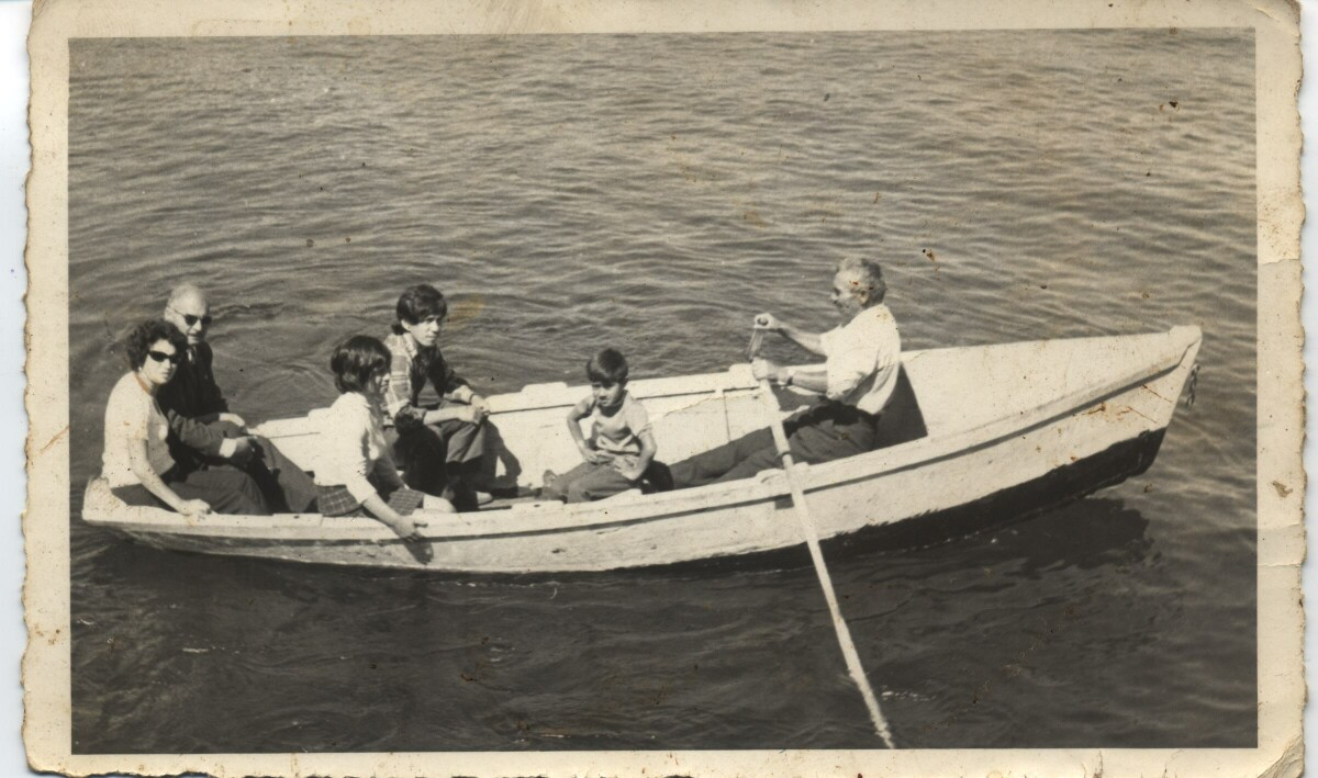 Plano entero de Hombres, una mujer, una niña y un niño en el interior de un bote. Un hombre mayor va remando mientras pasean por Lago Ranco