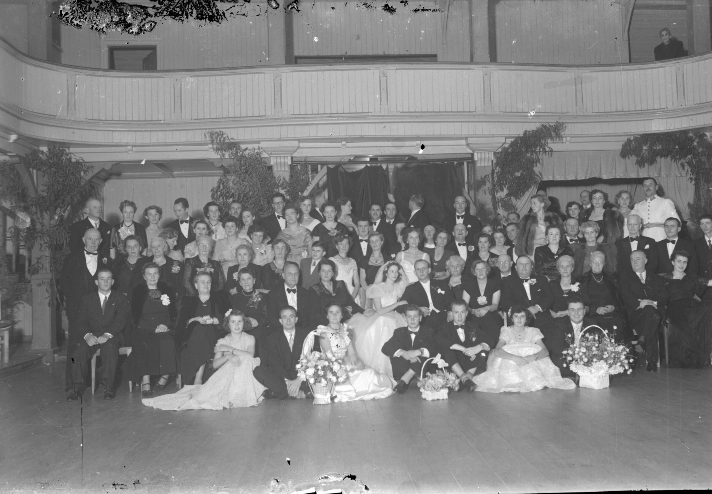 Plano general de un grupo de personas posando para un retrato grupal junto a una pareja de recién casado, sentados al centro del grupo