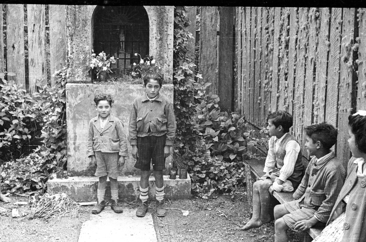 Plano general de dos niños posando de pie frente a un altar, a su alrededor, dos niños y una niña observándolos.