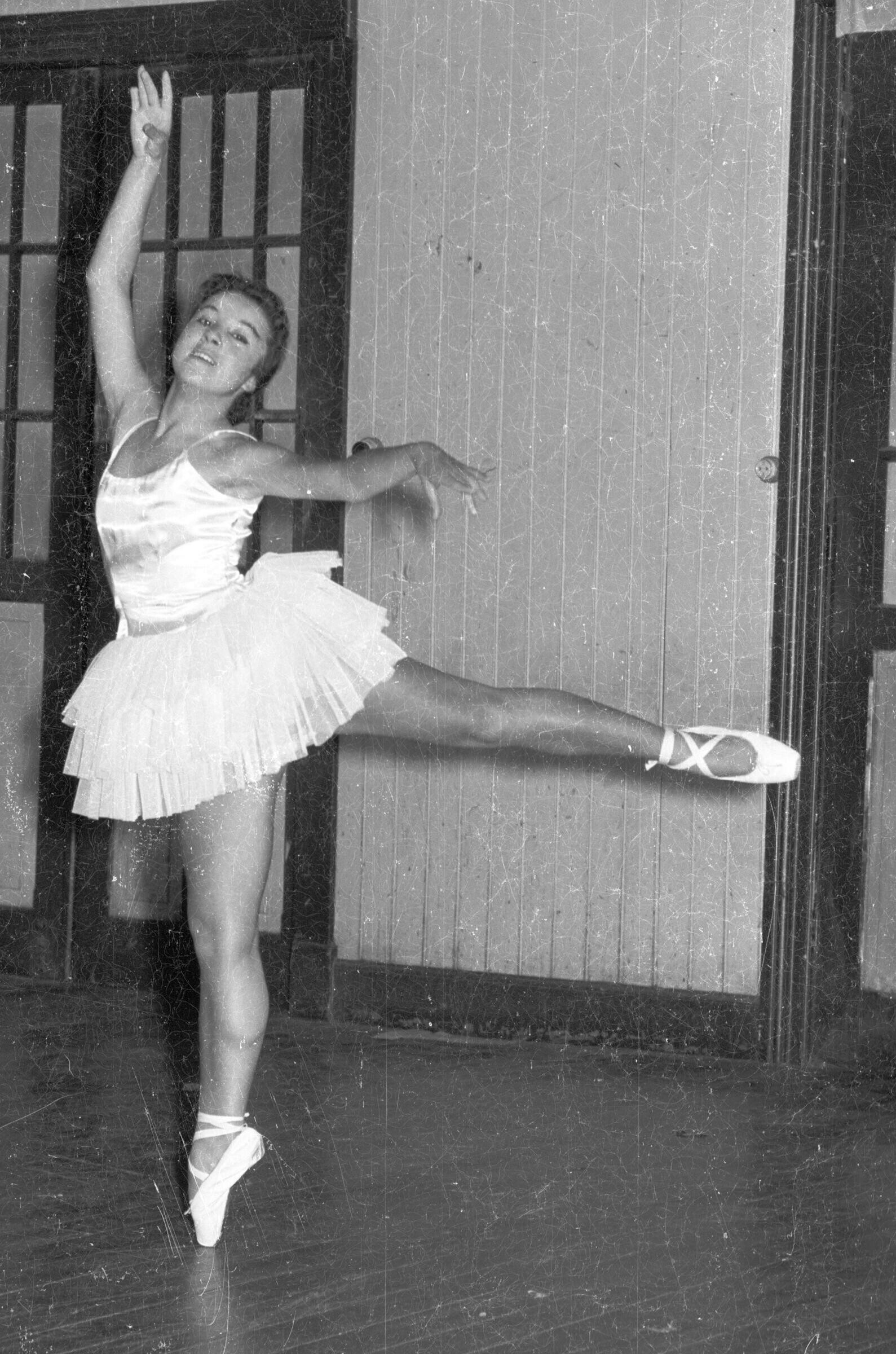 Retrato de plano entero de una mujer joven formada en una pose de ballet. Se encuentra en el interior de un lugar no identificado