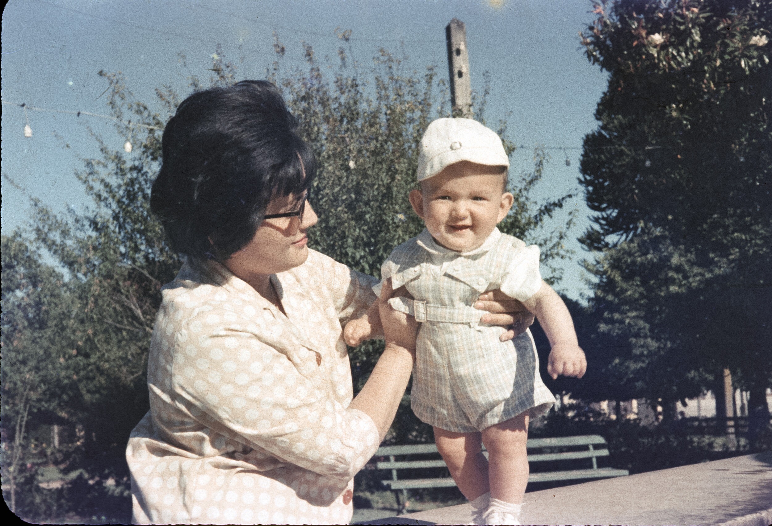 Retrato de plano medio de Mujer con Blusa sosteniendo a niño de temprana edad con jardinera corta y gorro parado sobre el borde de la pileta de Plaza de la Concordia