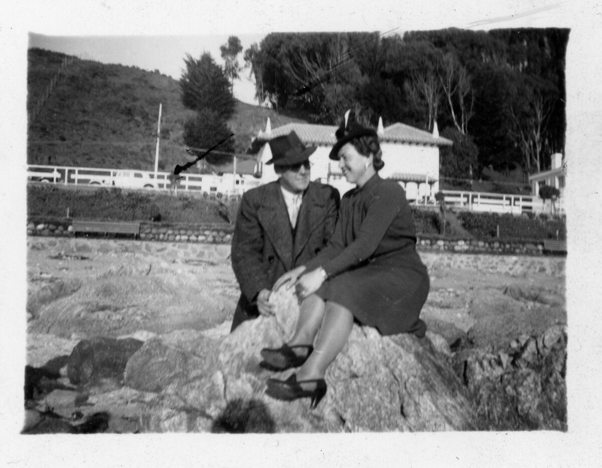 Retrato de plano entero de una pareja posando sentadas sobre unas rocas, durante un paseo realizado a una playa no identificada