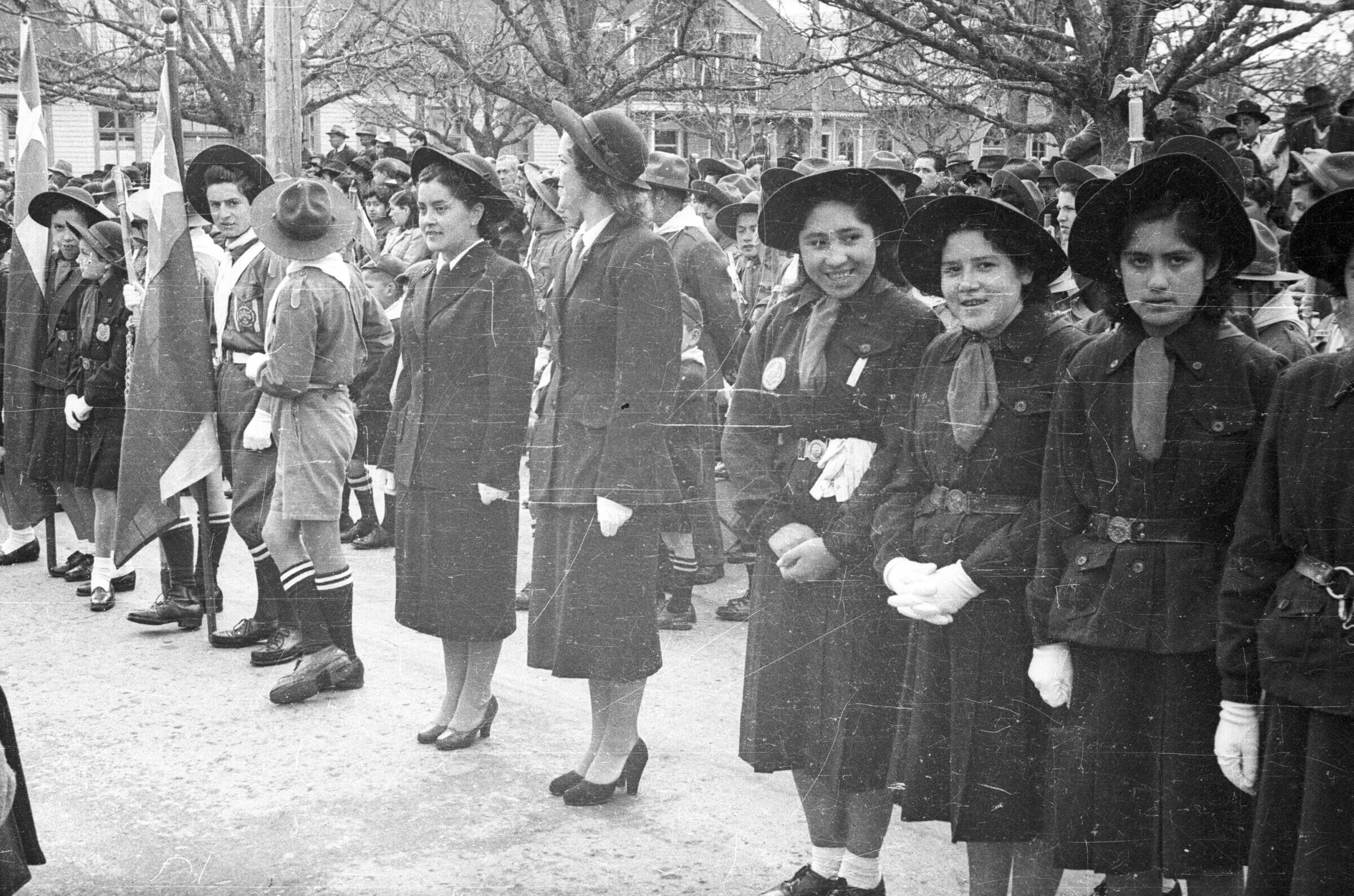 plano general de un grupo de Mujeres, Hombres, Niños y Niñas, algunos se encuentran de pie y otros están en las ventanas observando a un grupo de niñas scout cantando en la entrada de la Municipalidad de La Unión