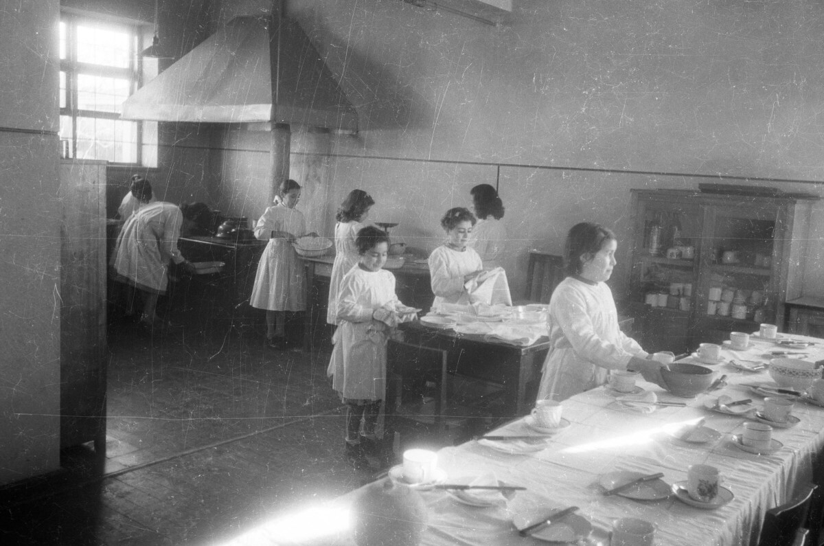 plano general de un grupo de niñas durante una clase donde se les enseña a cocinar y los quehaceres del hogar. Todas llevan un delantal blanco y se encuentran en el interior de la escuela superior de niñas Nº2 de La Unión