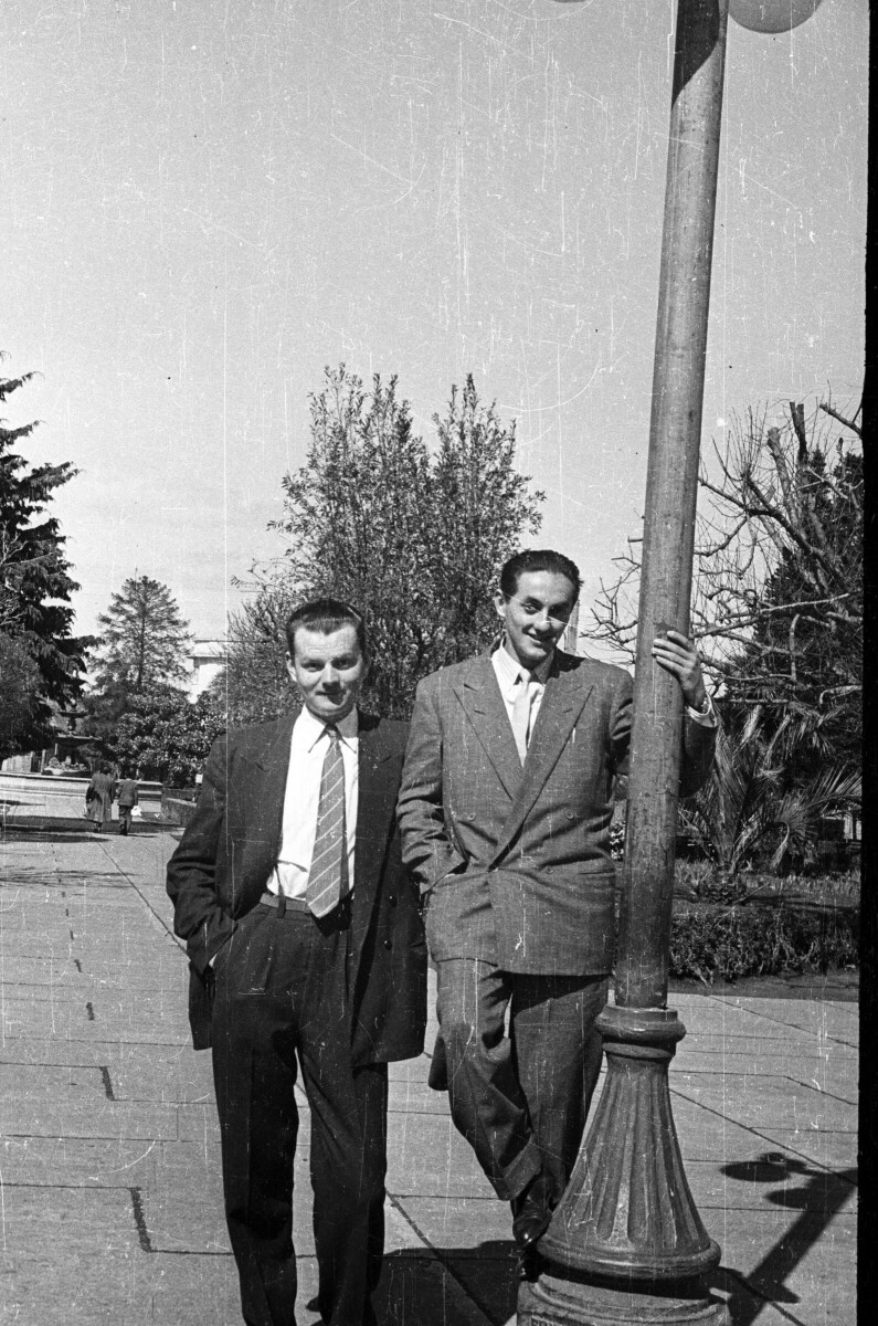 Retrato de plano entero de dos hombres posando, uno de ellos está afirmado en un poste de luz en la plaza de La Concordia en la Unión