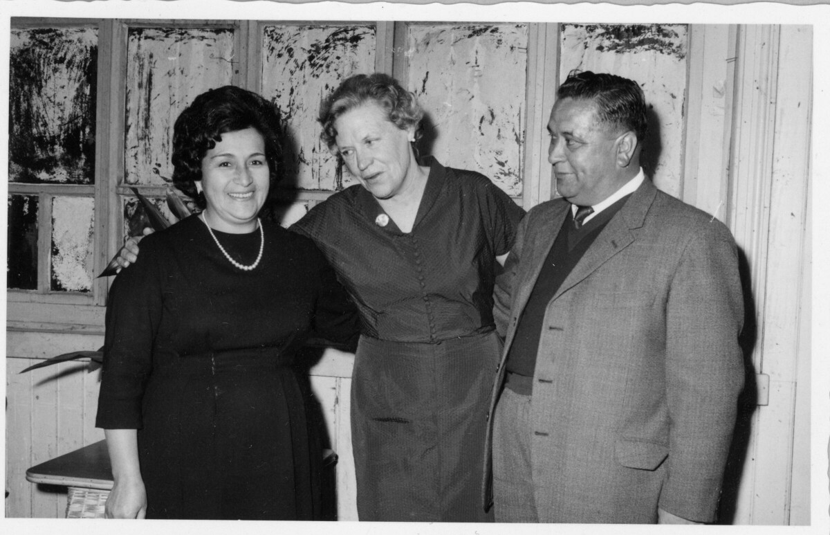 Retrato de plano medio largo  de Olga Boettcher posando junto a una mujer y un hombre. Se encuentran ubicados junto a una ventana, en el interior de un local no identificado durante  un banquete realizado en su honor, tras haber finalizado su gobernación