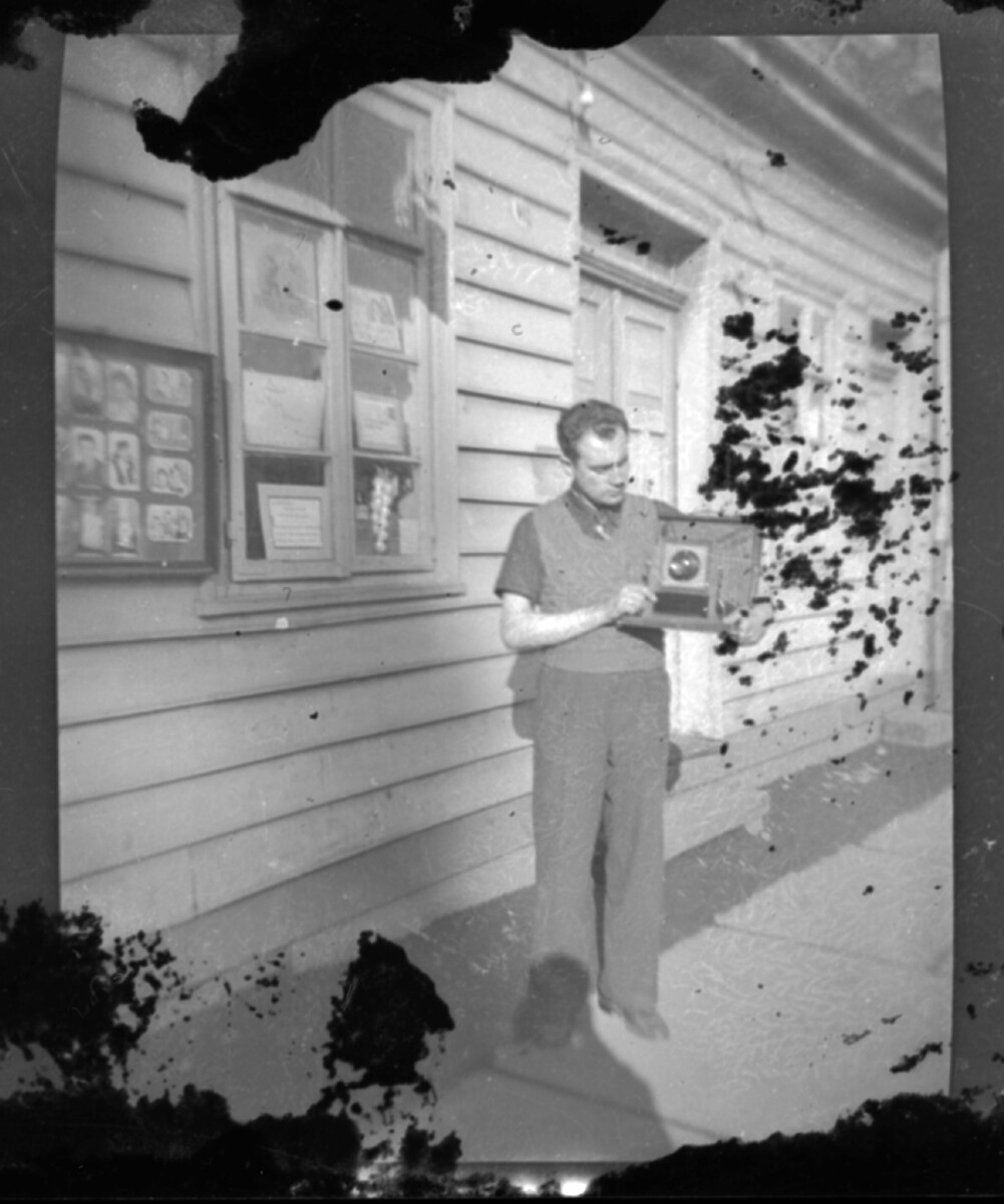 Plano entero de un hombre adulto sosteniendo una cámara fotográfica afuera de un estudio fotográfico