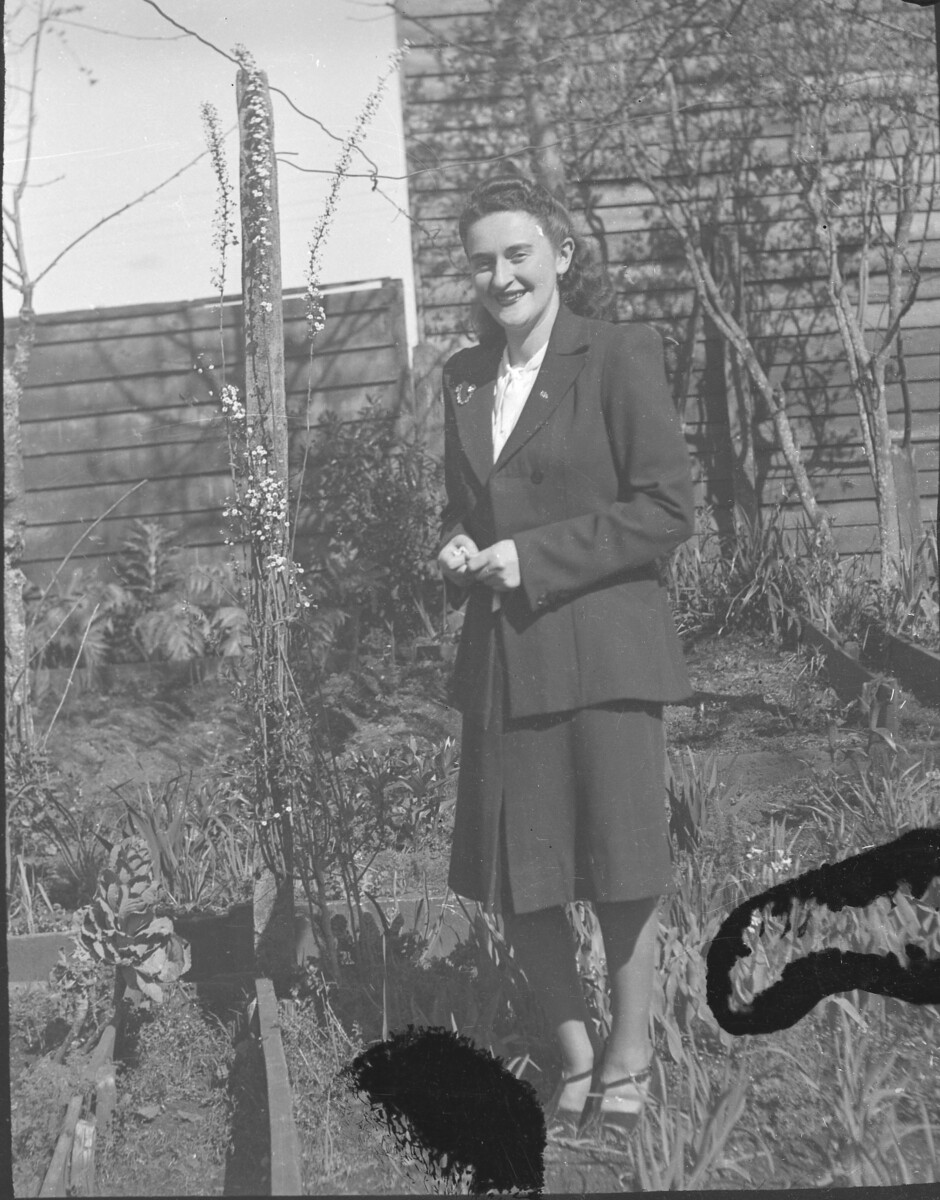 Plano entero de una mujer joven sonriendo entre las plantas de un jardín.
