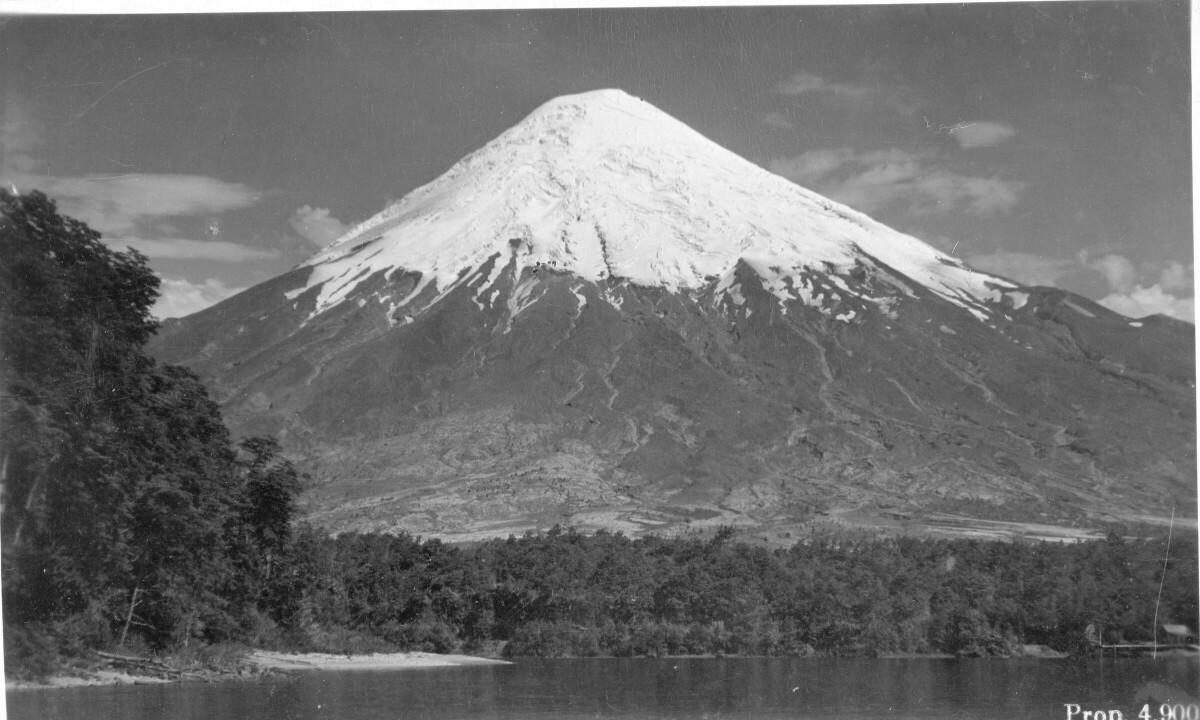 plano general de un volcán nevado no identificado. A sus pies hay un lago rodeado por bosque nativo