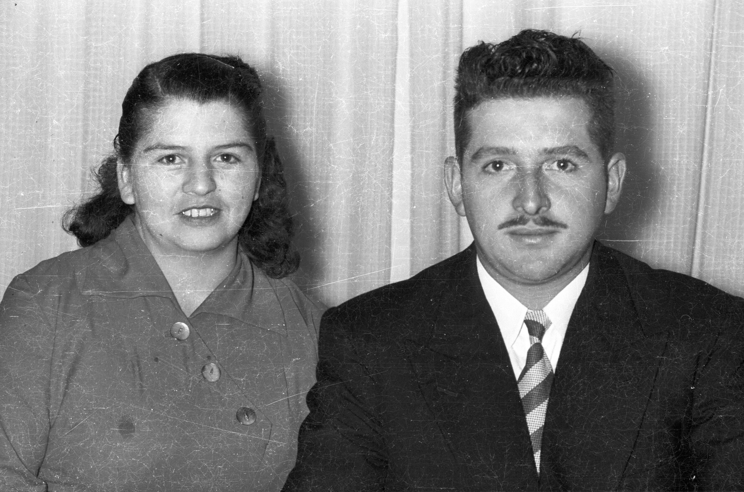 Retrato de plano medio de una mujer y un hombre posando por delante de una cortina en el interior de una casa