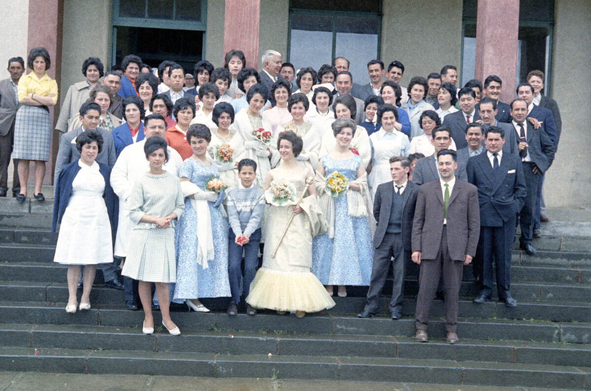 Retrato grupal de plano entero de Hombres, Mujeres, dos niños y la reina de la primavera posando sobre los peldaños de una escalera, en el frontis del Hospital Juan Morey de La Unión
