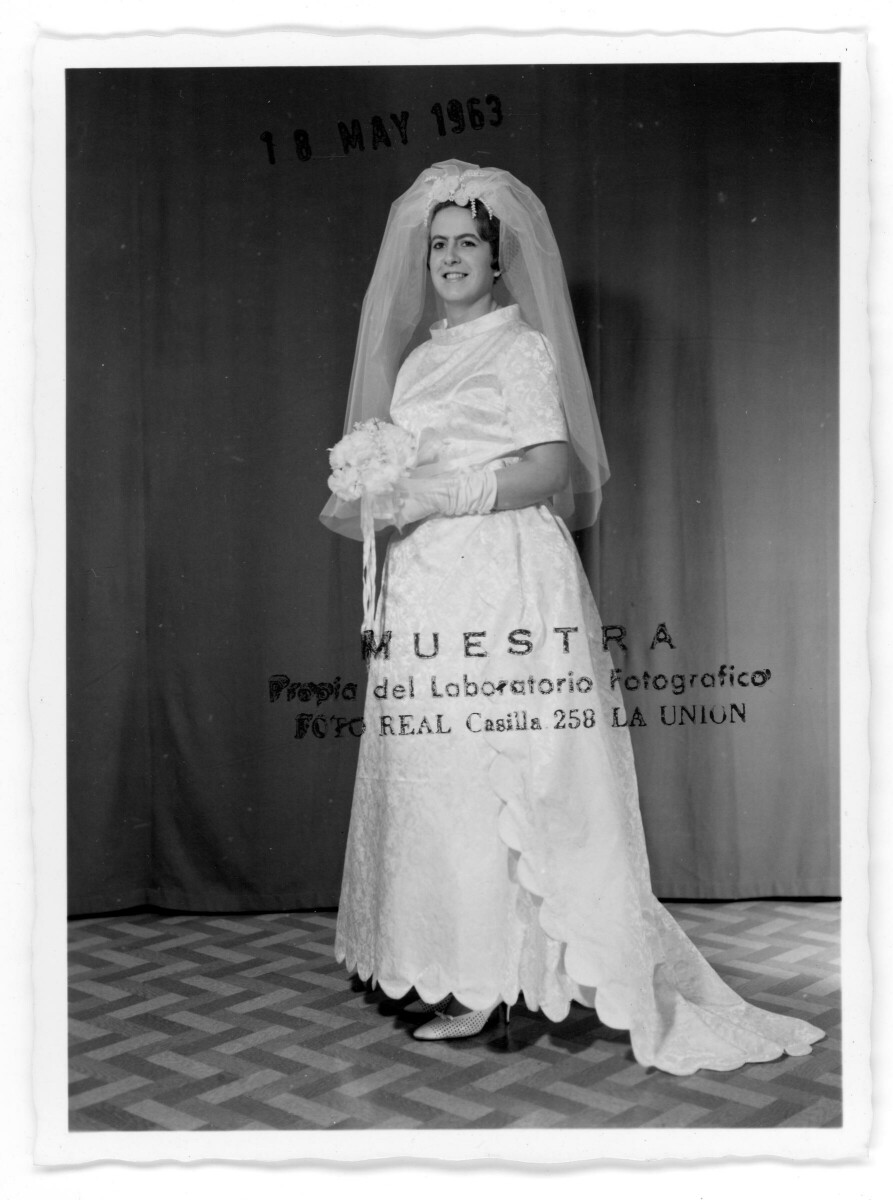 Retrato de estudio de Plano entero de María Eugenia Vergara vestida de novia, sonriendo mientras posa con un ramo de flores