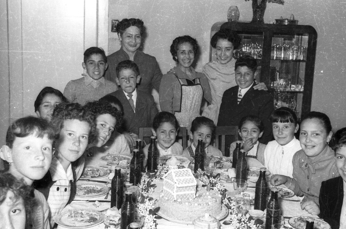 Retrato grupal de plano entero de Mujeres, niñas y Niños posando alrededor de una mesa mientras celebran una fiesta de cumpleaños en el comedor de una casa
