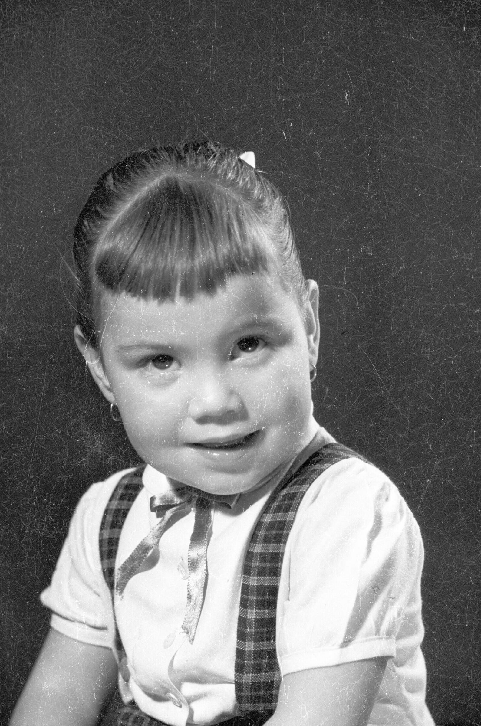 Retrato de estudio de plano medio mirando hacia arriba mientras posa sentada. Lleva el pelo recogido hacia atrás por un mono y usa flequillo