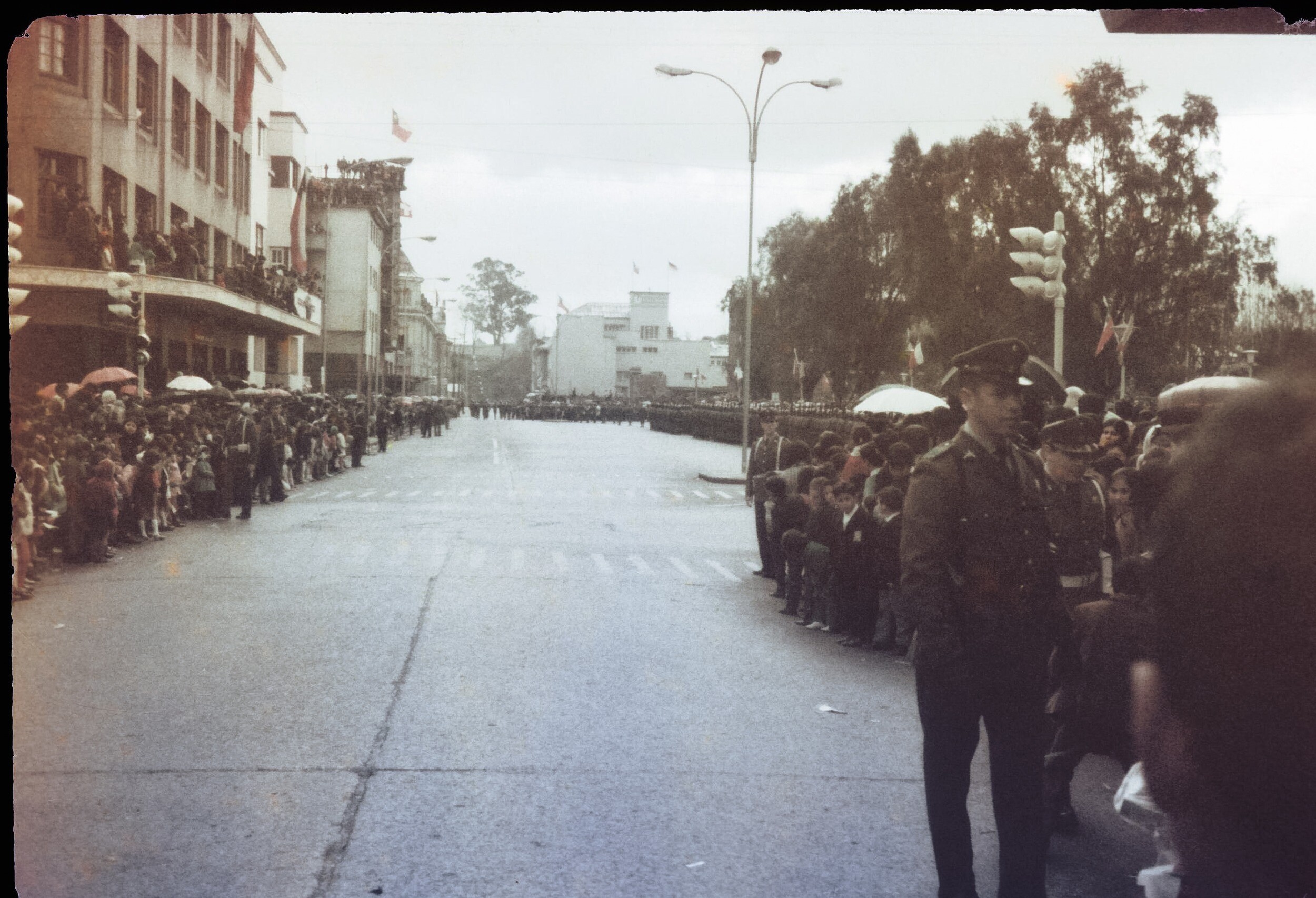 Plano entero de gran cantidad de personas ubicadas a los costados de una calle esperando a que pase un desfile en plaza de armas de Osorno