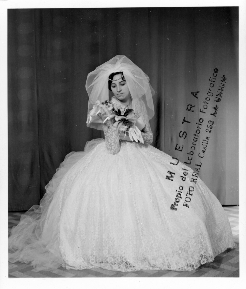 Retrato de estudio de Plano entero de una mujer vestida de novia, posando sentada mientras levanta su ramo de flores con ambas manos