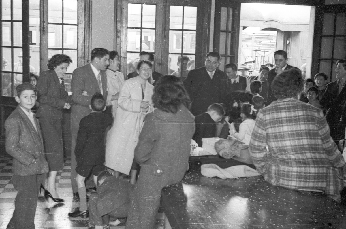 plano general de un grupo numeroso de Mujeres, Hombres, niñas y Niños reunidos en la entrada de la estación de trenes de La Unión