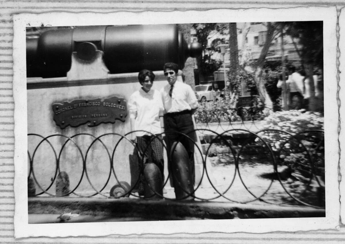 Retrato de un hombre y una mujer junto a un monumento al Coronel Francisco Bolognesi. Están en una plaza.