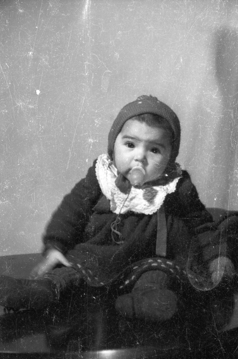 Retrato de estudio de Plano entero de Bebé con Vestido y gorro, sentada en una mesa, con chupete en la boca
