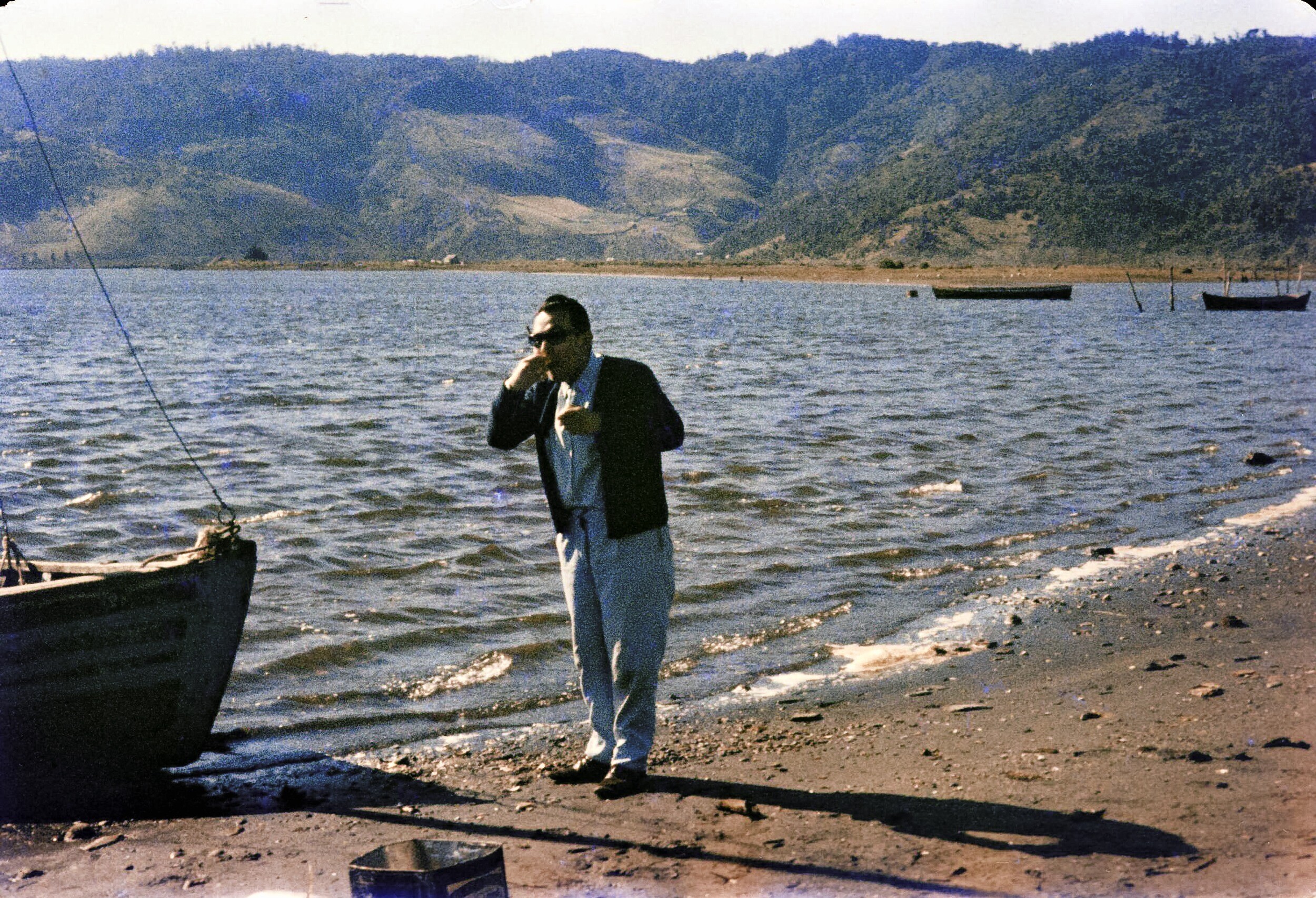 Retrato de plano entero de Hombre comiendo al borde de un lago con un bote varado