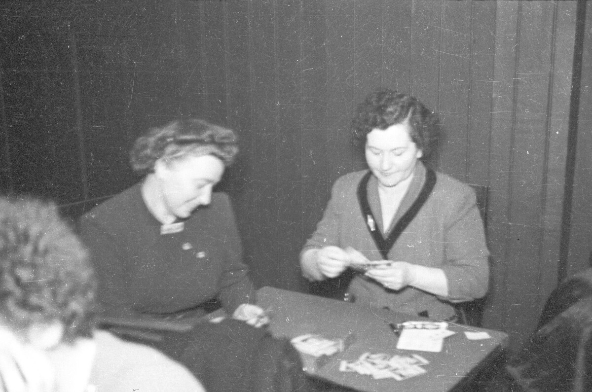 Plano entero de dos mujeres jugando al naipe sentadas en una mesa en el interior de un local