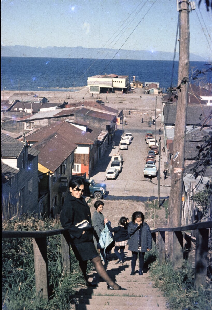 Retrato de plano entero de dos mujeres con Vestido junto a dos niñas posando en la escalera de una ciudad con una playa al fondo