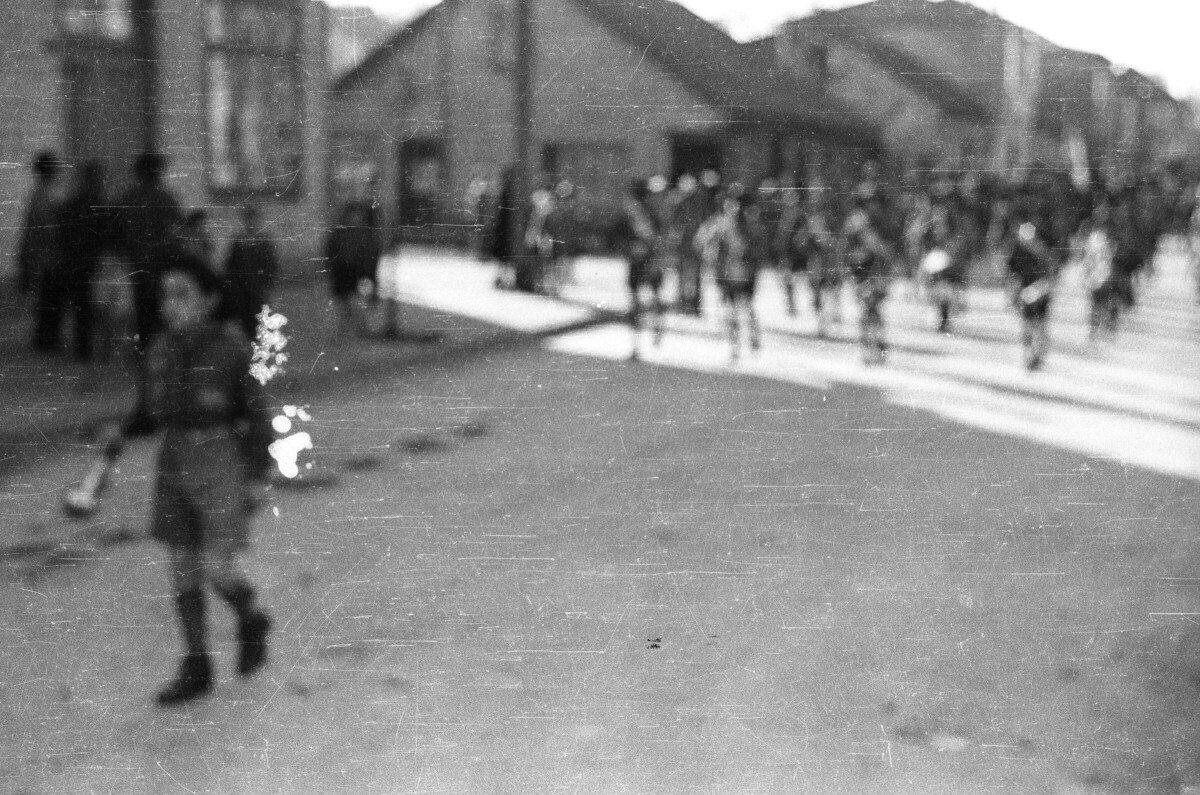 plano general de un niño caminando a metros de distancia de una brigada de scout que le sigue formados en hileras mientras desfilan por una de las calles de la ciudad de La Unión