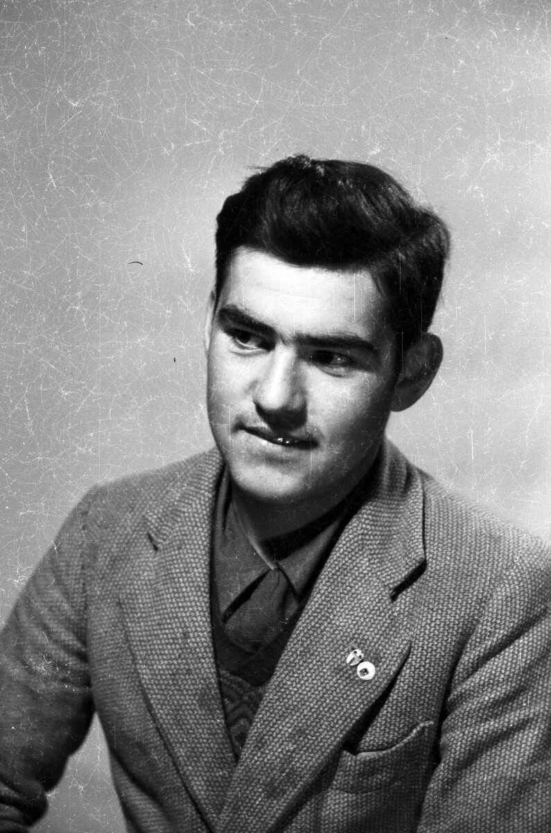 Retrato de estudio de Plano medio de un hombre posando de Medio perfil. Lleva puestas dos piochas en la solapa de su Traje