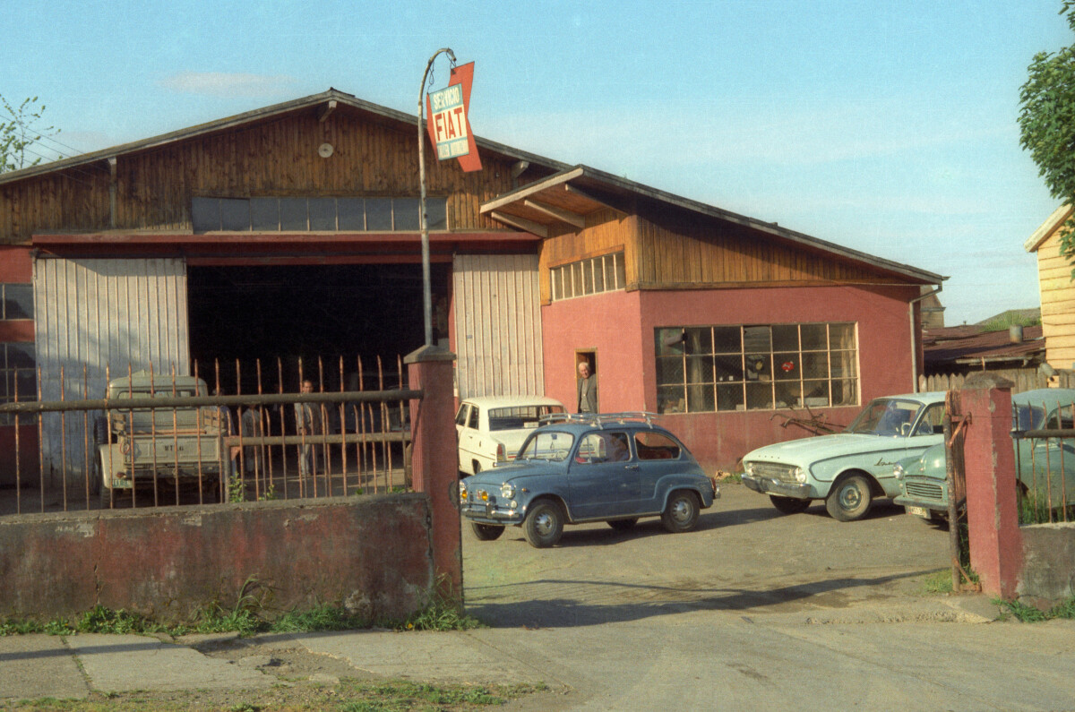 Plano general de la entrada del taller automotriz -servicio Fiat- tipo galpón, con numerosos autos y camionetas estacionados en la entrada