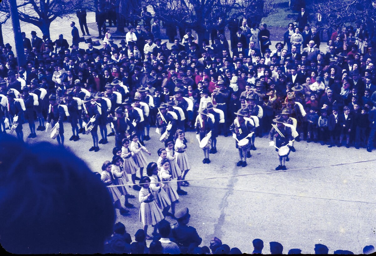 Plano entero vista superior de banda escolar tocando mientras un grupo de niñas desfila por calle Prat frente a Plaza de la Concordia de La Unión