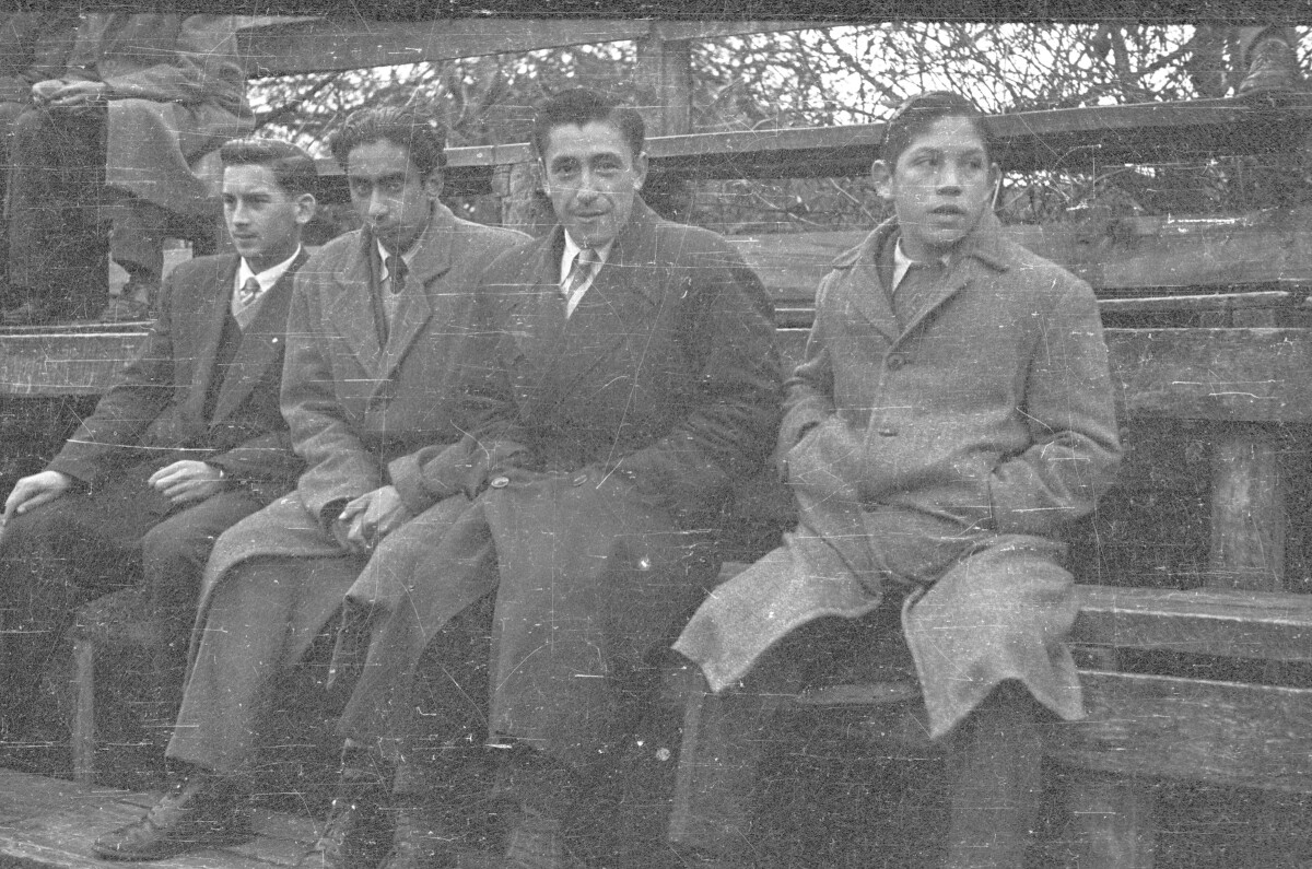 Plano entero de cuatro hombres sentados en las graderías observando un partido de básquetbol femenino