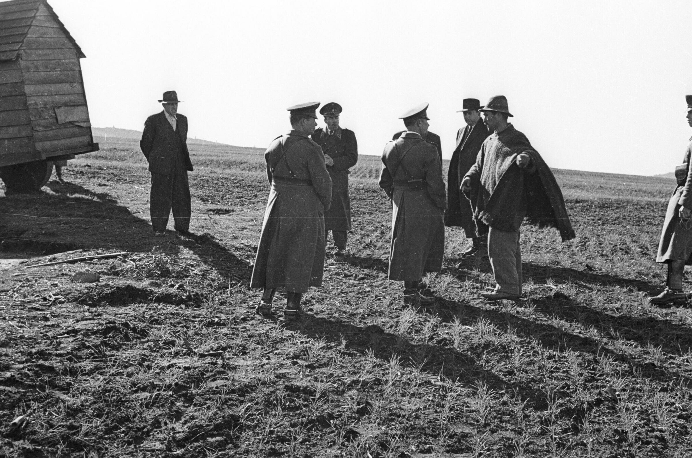 Plano entero de un carabinero conversando con un hombre de sombrero y manta, mientras a su alrededor otros uniformados y hombres vestidos de Traje los observan.