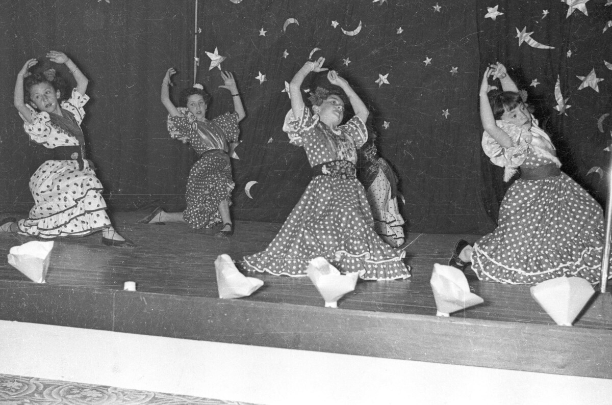 Plano entero de un grupo de Niñas bailando flamenco sobre el escenario ubicado en el gimnasio de la Escuela de Niñas Nº2