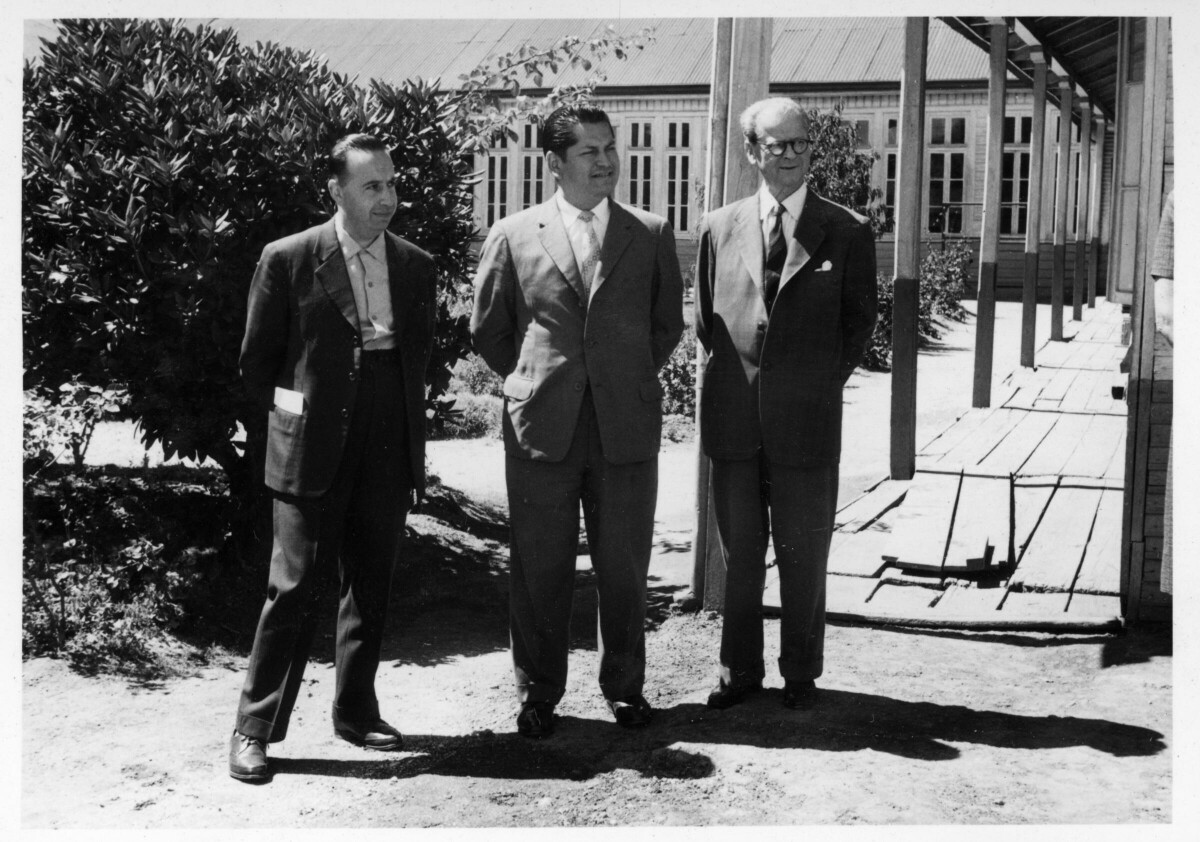 Plano entero de tres hombres parados junto al pasillo de una infraestructura no identificada durante la visita de Olga Boettcher al lugar