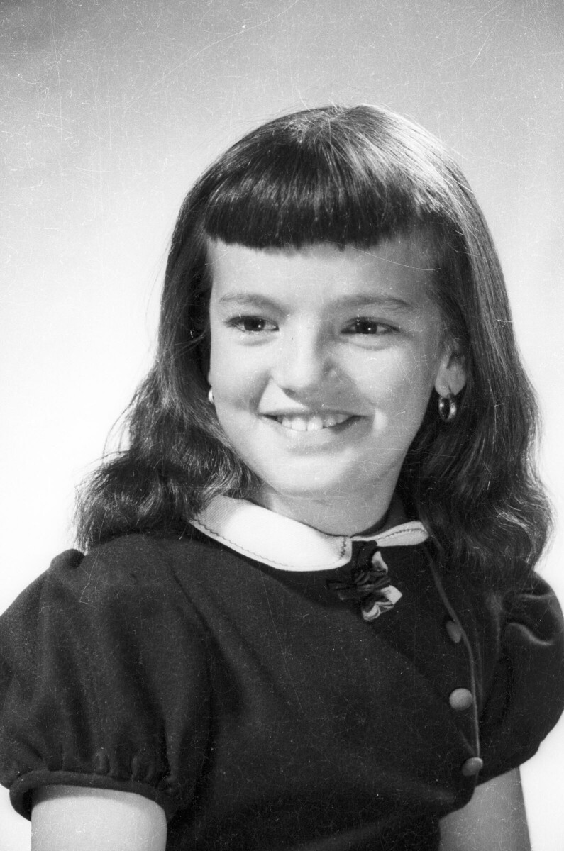 Retrato de estudio de una niña sonriendo mientras posa de Medio perfil. Lleva puesto un Vestido y usa chasquilla